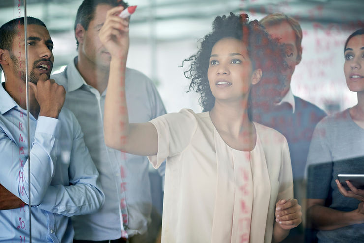 Woman working on a board planning while male colleagues stand around and understand. 